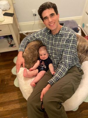 Young Audiences Executive Director Cary Clarke sitting in a chair with his baby daughter Sadie